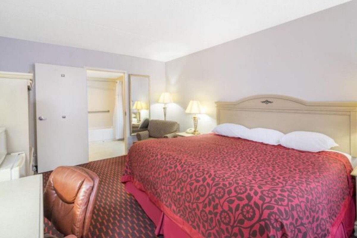 A hotel room with a bed, two bedside lamps, a chair, and a door leading to another room.