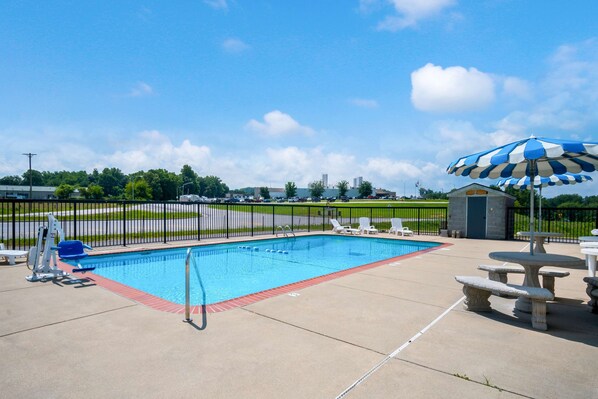 A rectangular swimming pool with a red edge, surrounded by a black fence, and a blue and white striped umbrella.