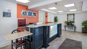 A reception area with a counter, seating, a plant, and a mirror. - Motel 6 London, KY (London)