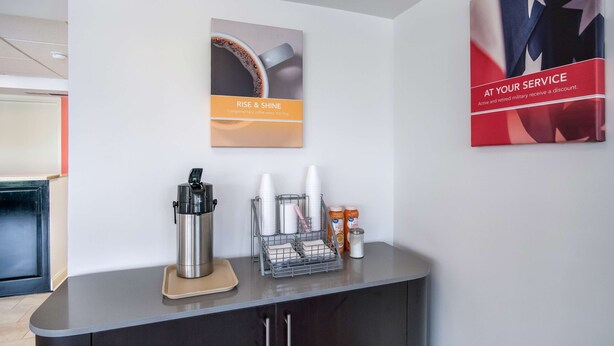 A reception area with a coffee station, a framed poster, and a wall-mounted sign. - Motel 6 London, KY (London)