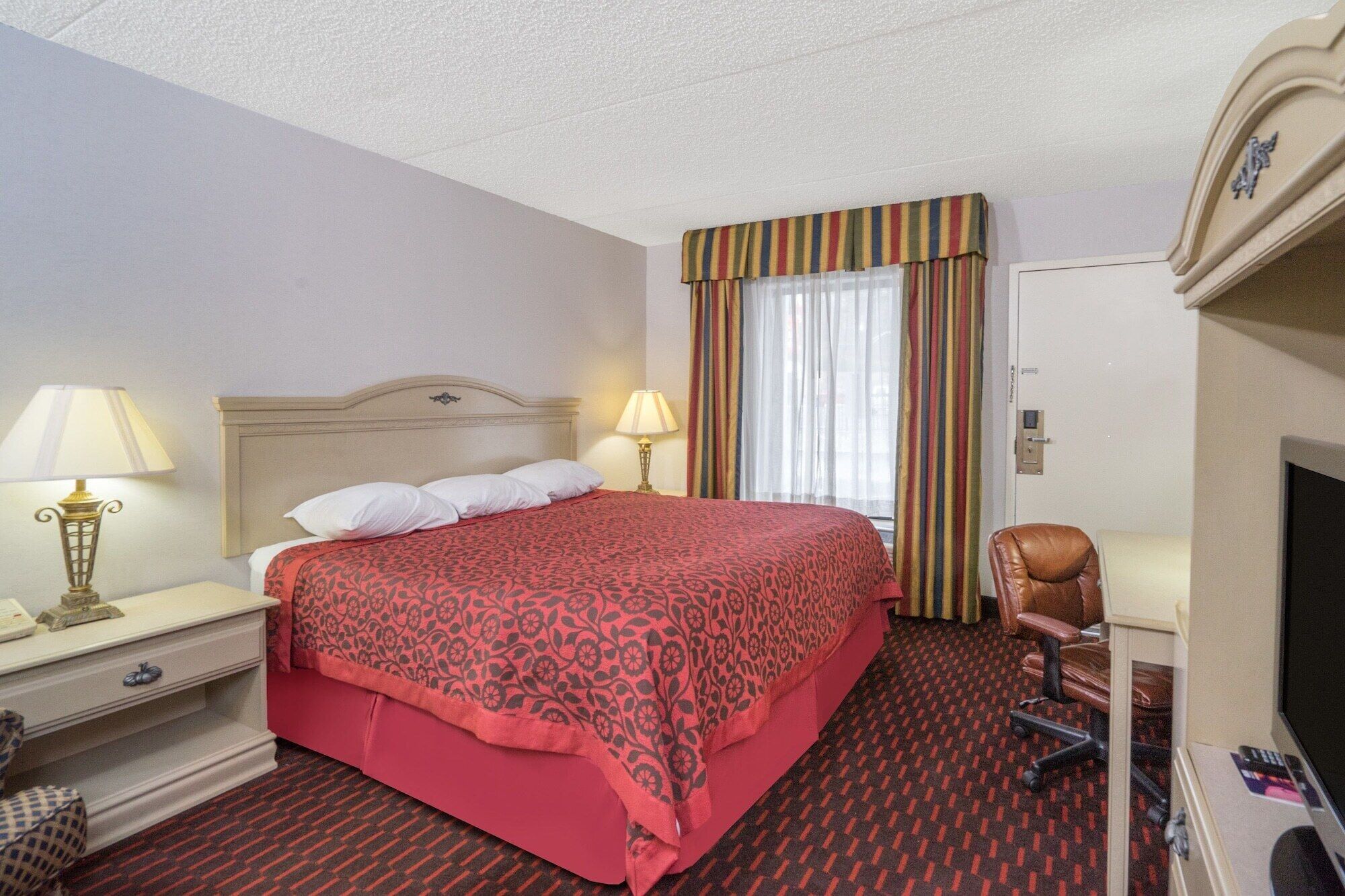 Una habitación de hotel con una cama, dos lámparas de noche, una silla, un televisor y una puerta.