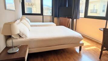 A hotel room with a bed, bedside table, lamp, TV, and large windows.