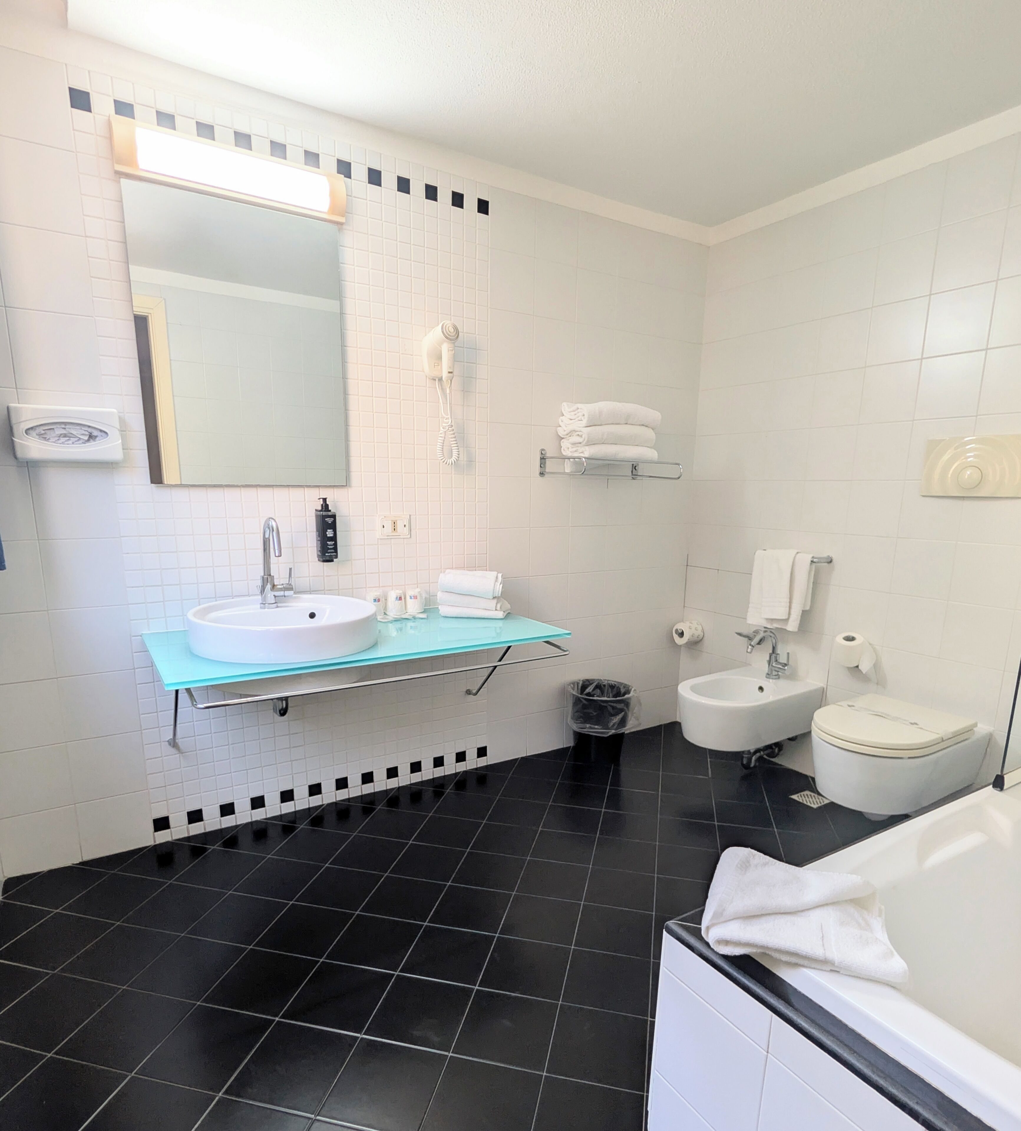 A modern bathroom with a glass vanity, a white sink, a mirror, a white toilet, and a bidet.