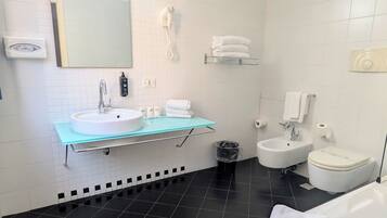 A modern bathroom with a glass vanity, a white sink, a mirror, a white toilet, and a bidet.
