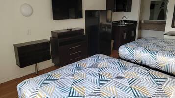 A bedroom with two beds, a TV, a refrigerator, and a small kitchenette.