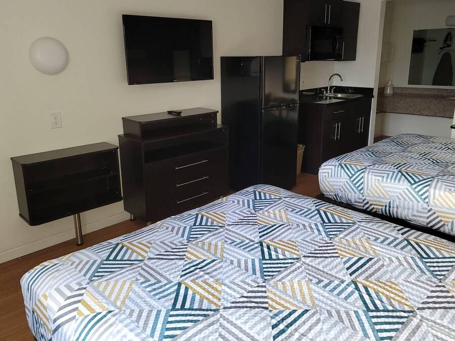 Un dormitorio con dos camas, televisor, refrigerador y una pequeña kitchenette.