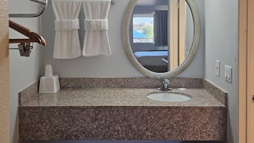 A bathroom with a granite countertop, a white sink, a round mirror, and two towels hanging on a towel rack.