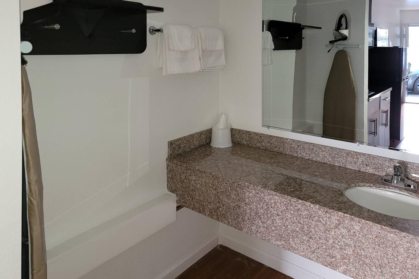 A bathroom with a granite countertop, a sink, and a mirror. There are towels hanging on a rack and a black bag on the wall.