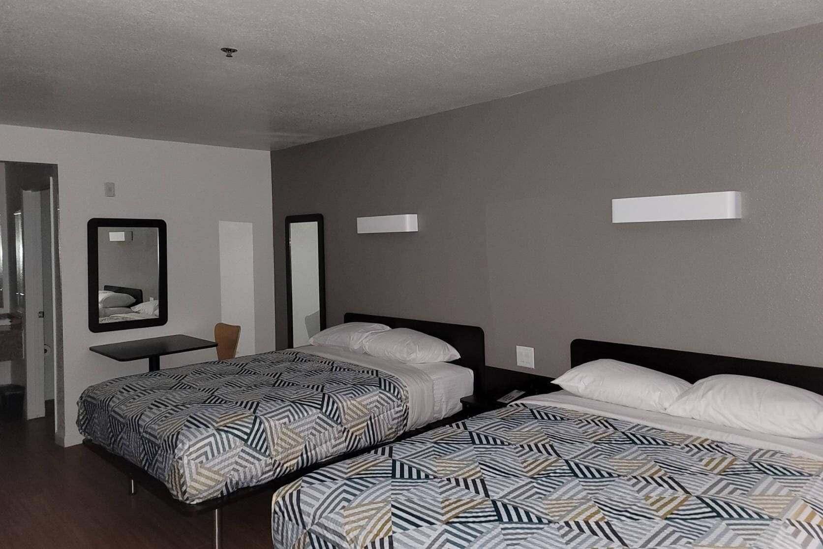 Ein Hotelzimmer mit zwei Betten, einem Schreibtisch, einem Stuhl und zwei Spiegeln.
