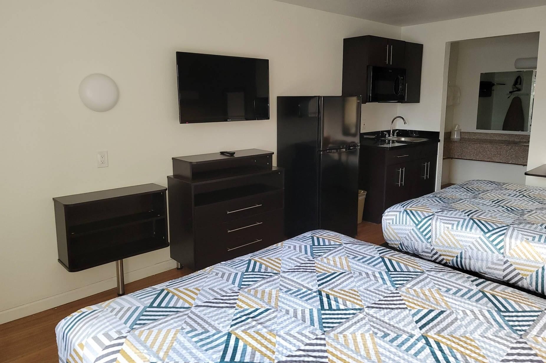 A compact room with two beds, a TV, a refrigerator, a microwave, and a small kitchenette.