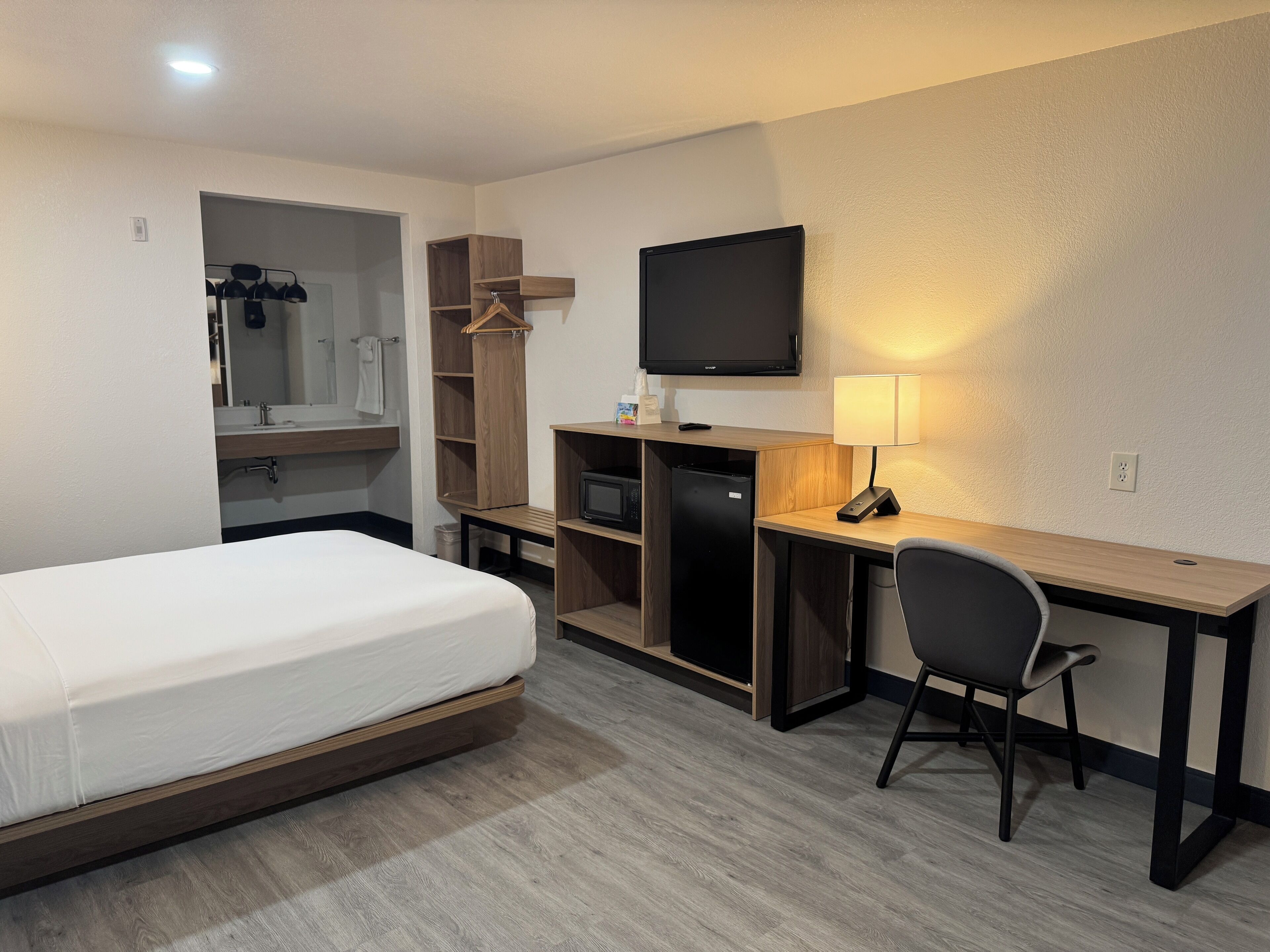 Een hotelkamer met een bed, een bureau met stoel, een televisie en een lamp.
