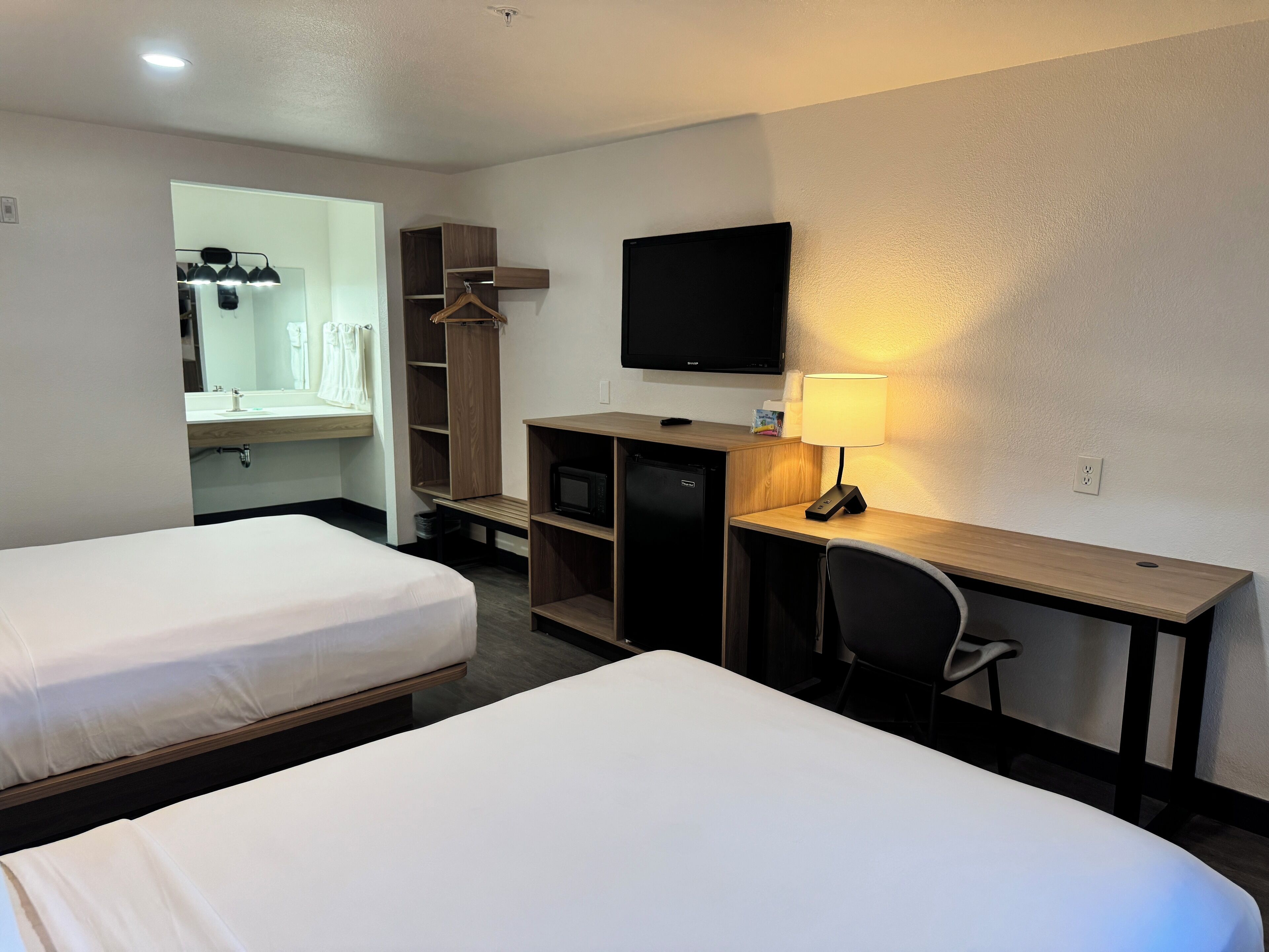 Une chambre d’hôtel avec deux lits, un bureau équipé d’un ordinateur et d’une lampe, une télévision et un dressing.