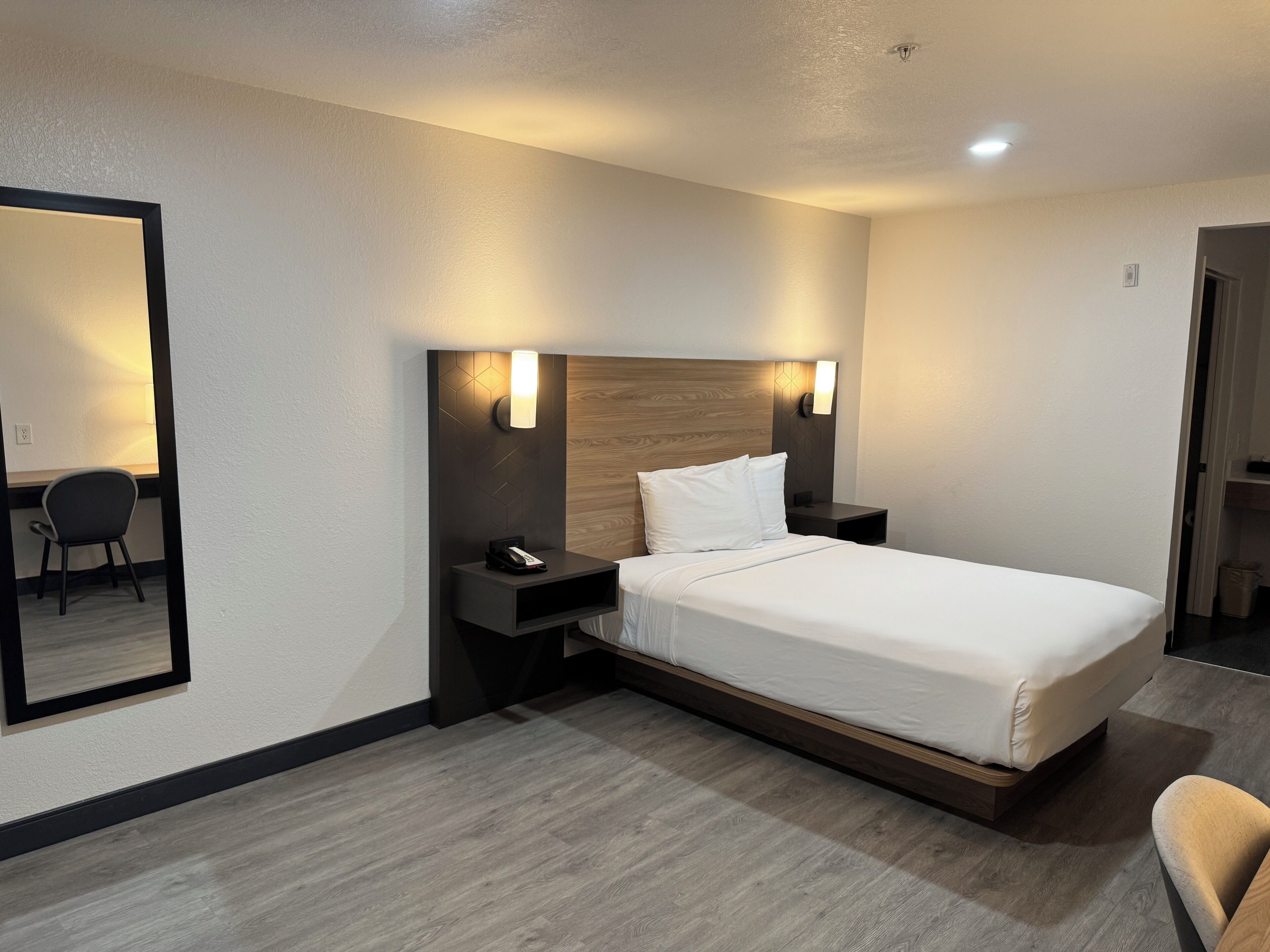 A hotel room with a bed, bedside tables, a desk, and a chair.