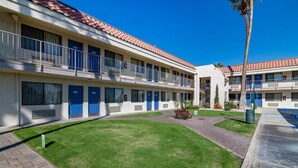 Un motel à étages, doté d’un toit recouvert de tuiles, de portes bleues et d’une pelouse bien entretenue.