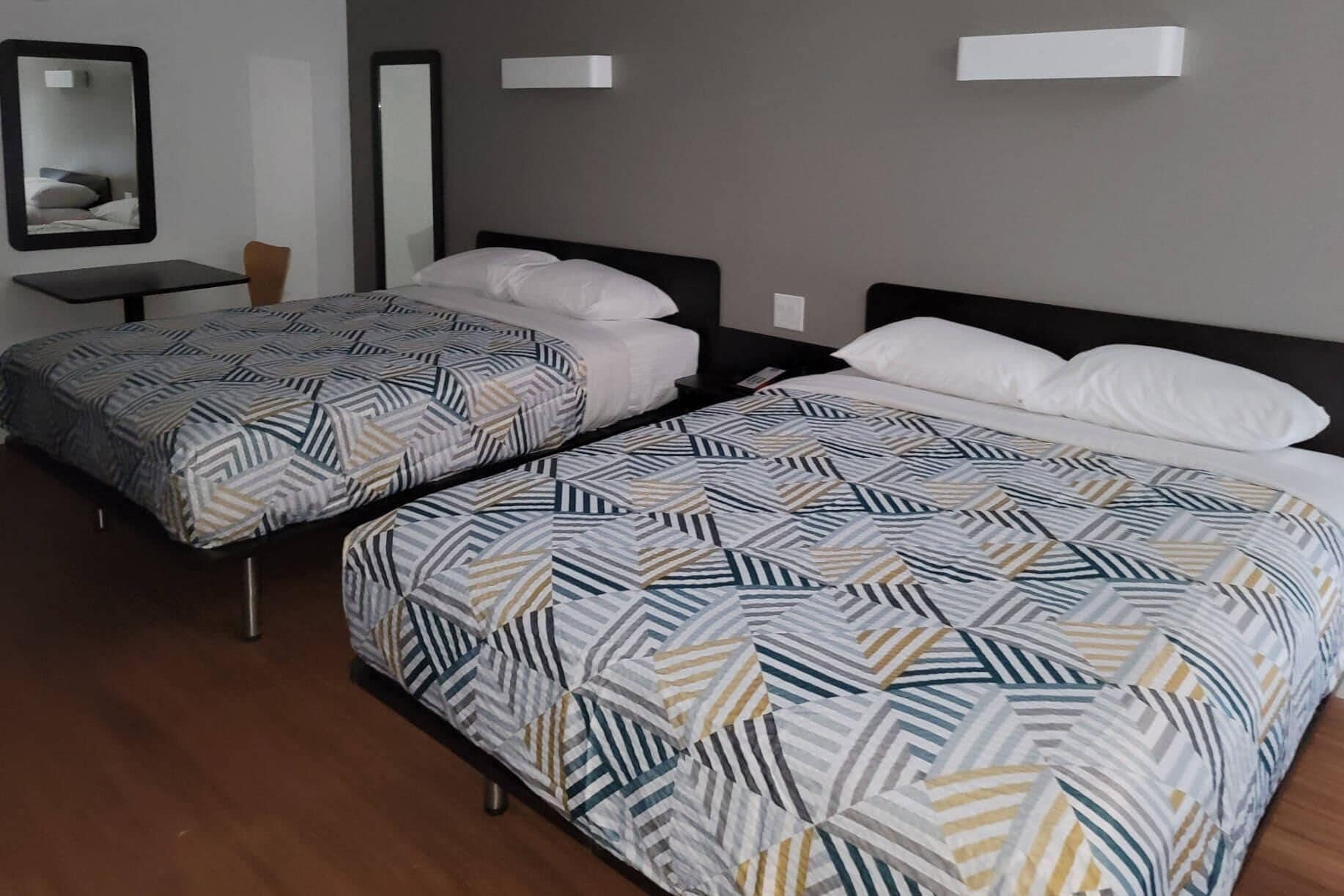 Habitación de hotel con dos camas, cada una con una colcha estampada, una mesita y una silla.