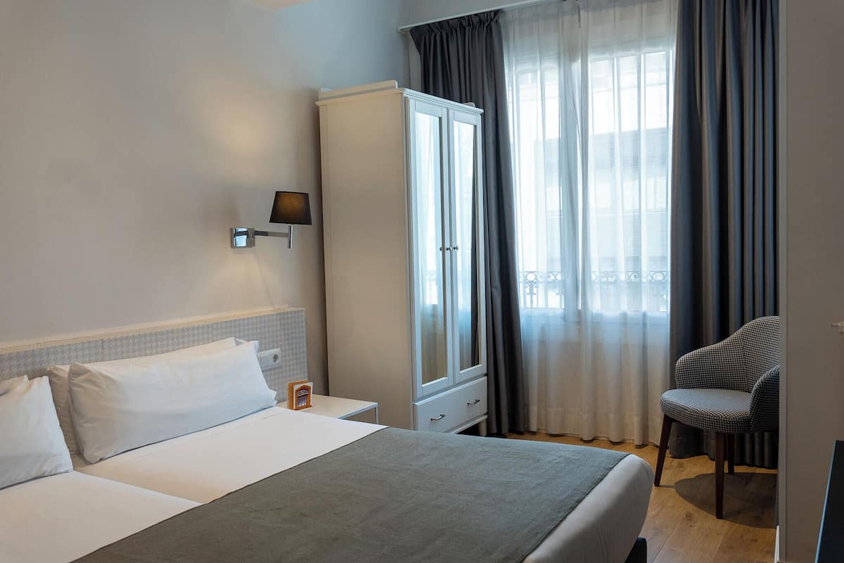 Ett hotellrum med en säng, en garderob, en stol och ett fönster med gardiner.