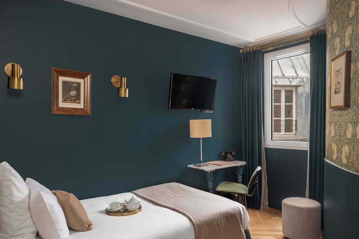 A neatly arranged bedroom with a bed, bedside table, lamp, and a television on the wall.