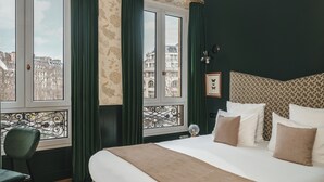 Ein Hotelzimmer mit einem großen Bett, grünen Vorhängen, Blick auf Gebäude und einem gemusterten Kopfteil.