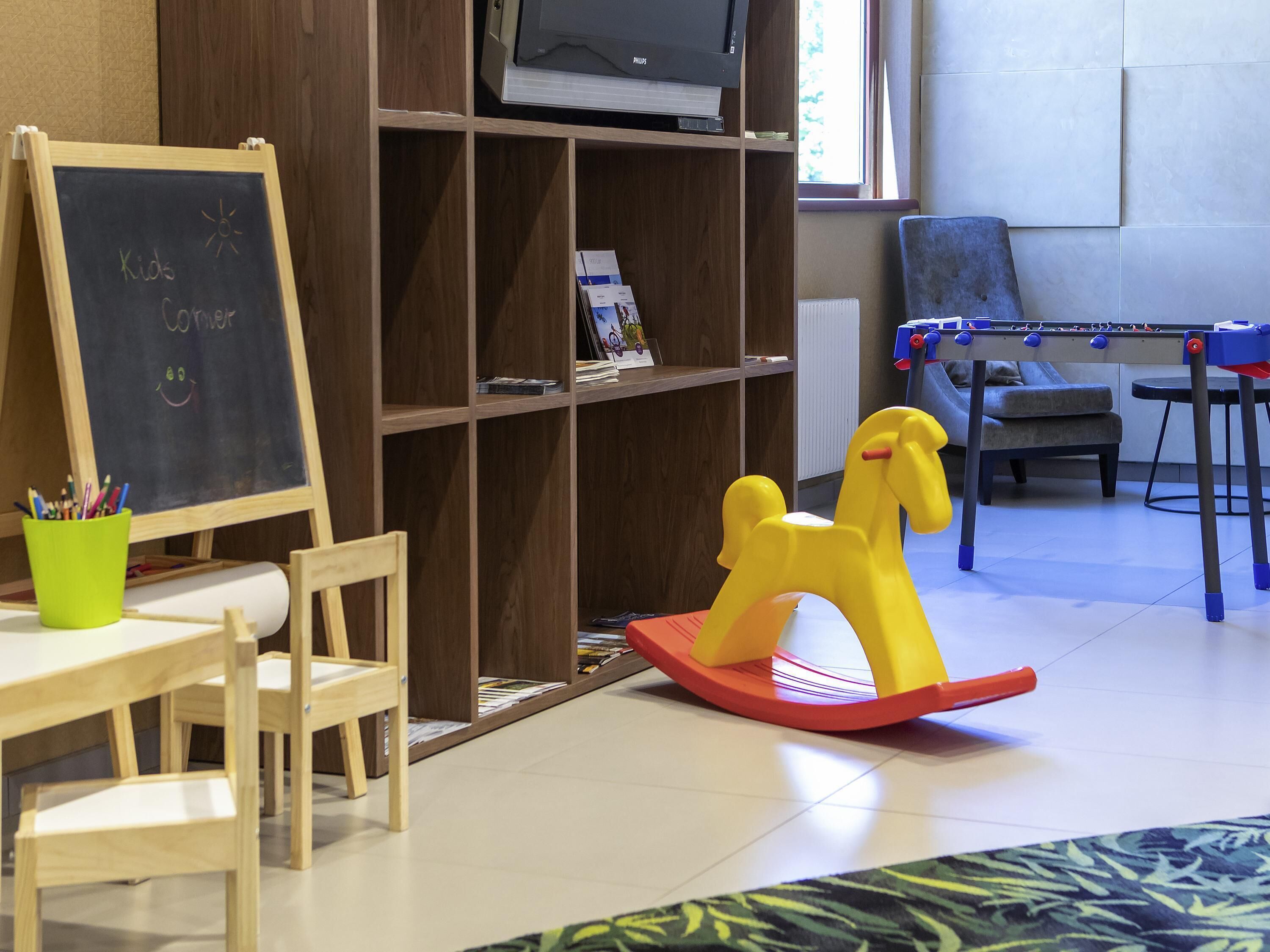 A children's corner with a chalkboard, a wooden table, chairs, a bookshelf, a television, a sofa, and a foosball table.