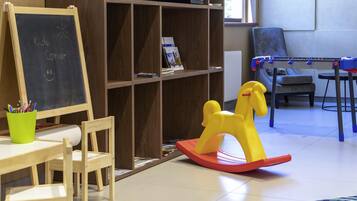 A children's corner with a chalkboard, a wooden table, chairs, a bookshelf, a television, a sofa, and a foosball table.