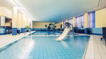 An indoor swimming pool with a slide, seating area, and a bar.