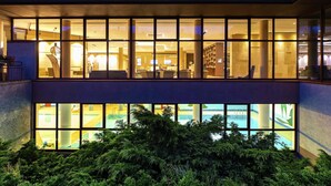 A hotel with a modern design, featuring large windows, a swimming pool, and a well-lit interior.