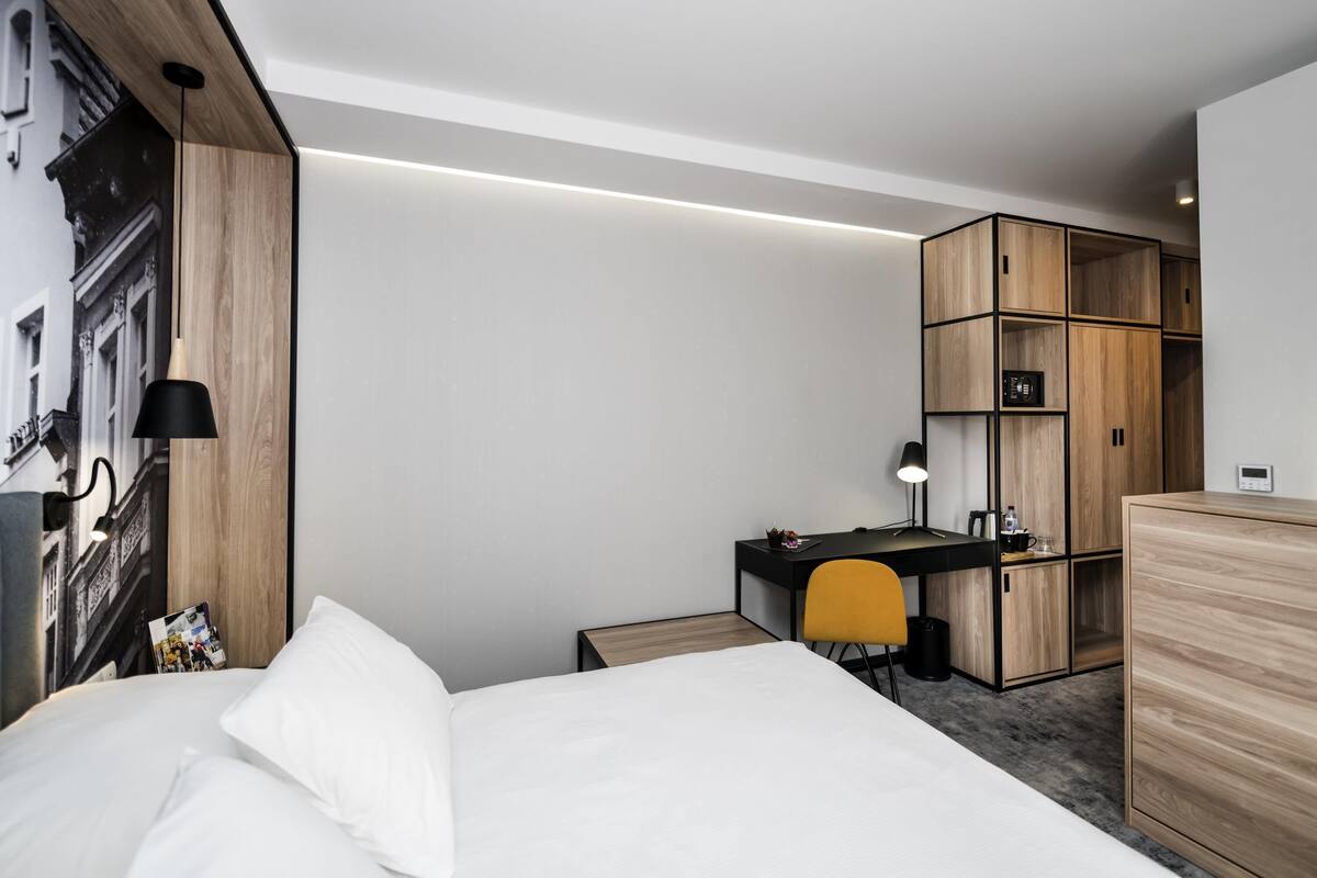 Ein modernes Hotelzimmer mit Bett, Schreibtisch, Stuhl und Kleiderschrank.
