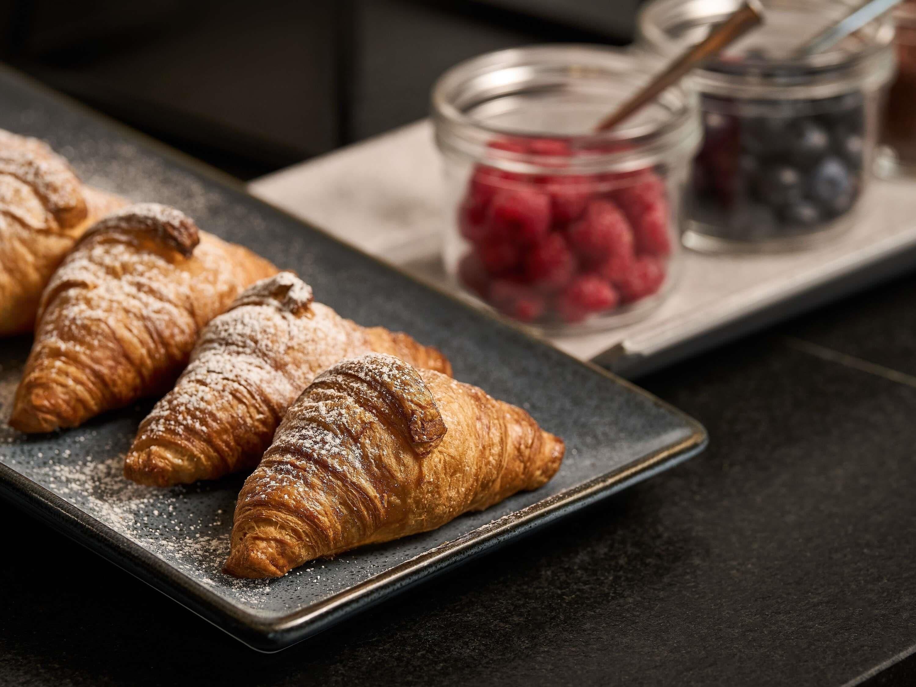 A tray with croissants and jars of berries.