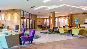 A modern hotel lobby with seating areas, a reception desk, and a large screen displaying information.