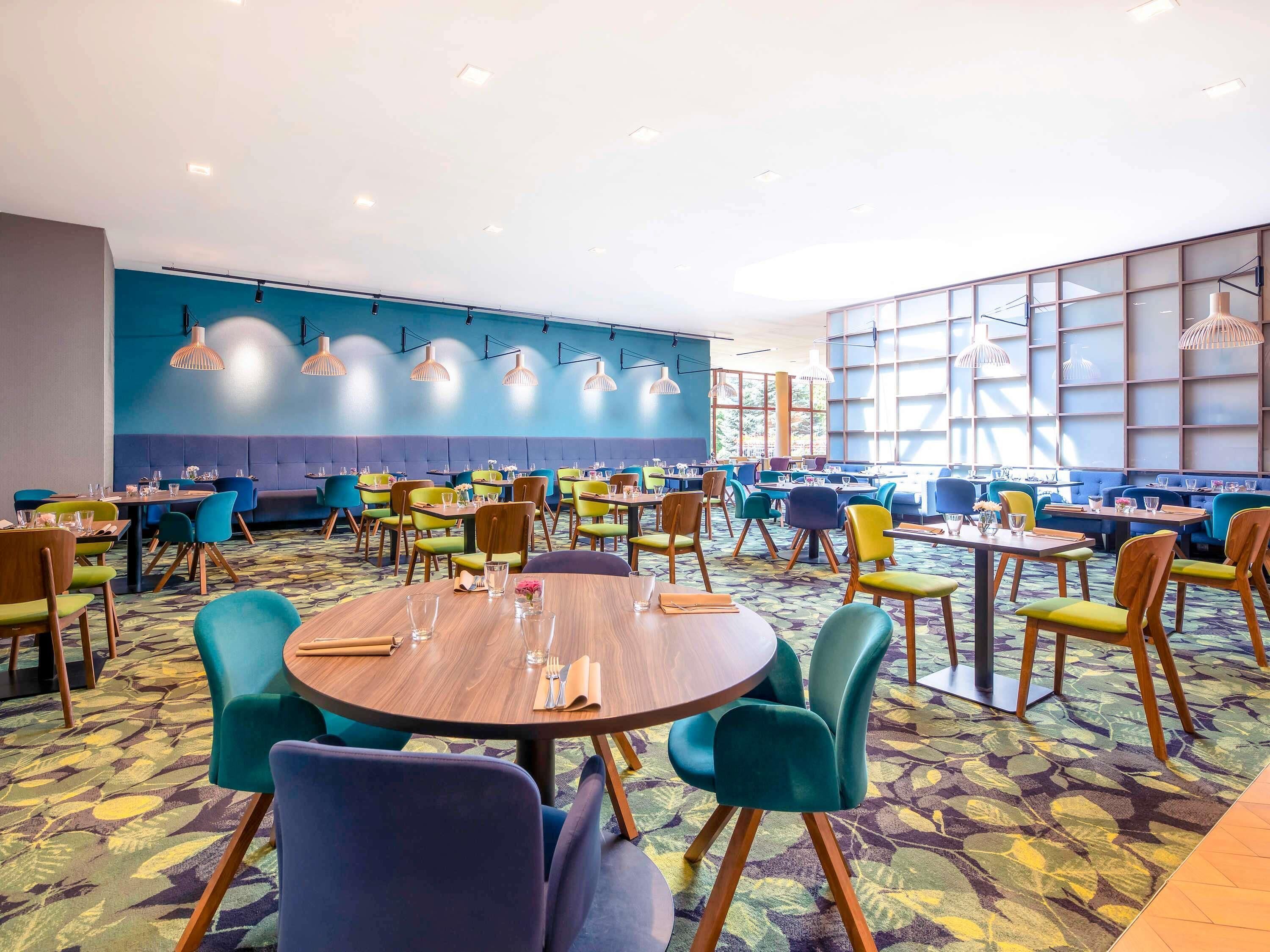 A restaurant with round tables, colorful chairs, and a patterned carpet.