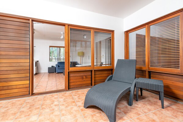 Una habitación con puerta corrediza de vidrio que da a una cocina, una butaca gris y una pequeña mesa.