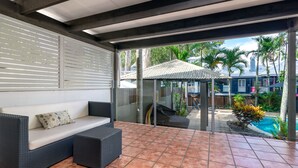 A covered patio with a sofa and outdoor seating, a tiled floor, and a view of a swimming pool and palm trees. - Paradise on the Beach Resort - Palm Cove (Palm Cove)