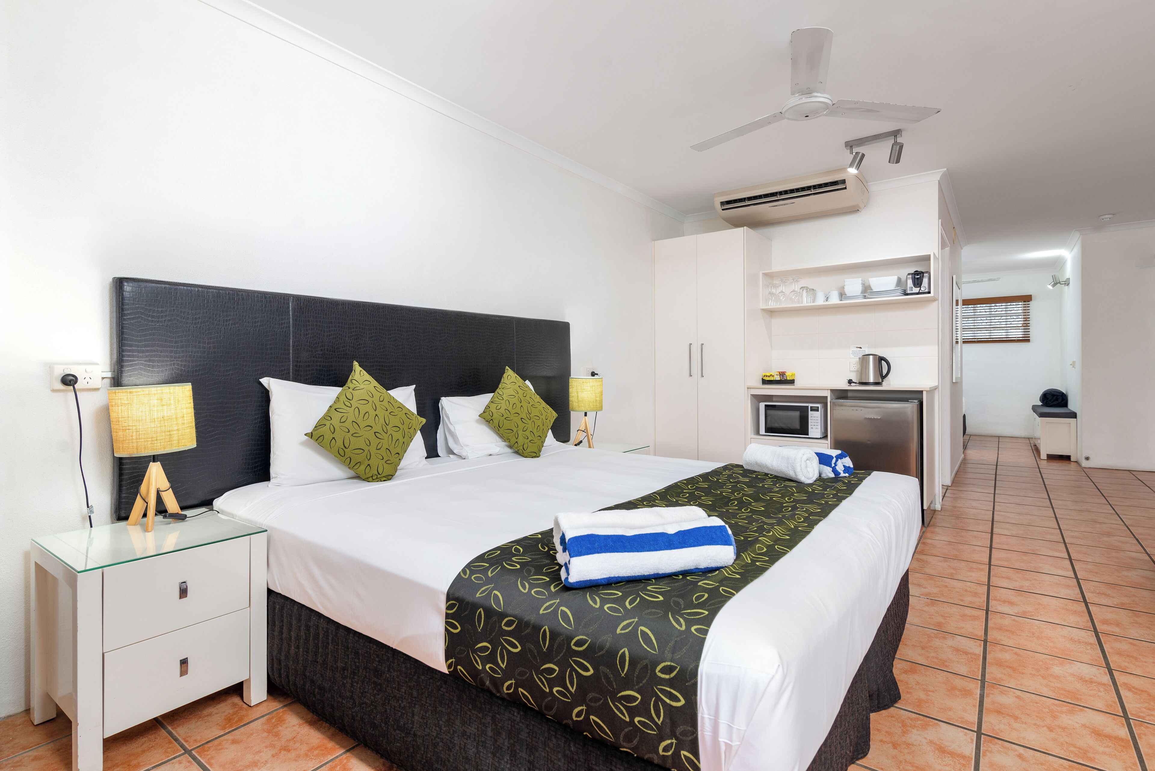 A hotel room with a bed, bedside tables, a desk, a microwave, and a ceiling fan.