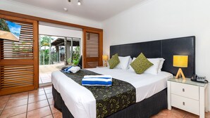 A hotel room with a large bed, a nightstand with a lamp, and a view of the outdoors through a sliding door. - Paradise on the Beach Resort - Palm Cove (Palm Cove)
