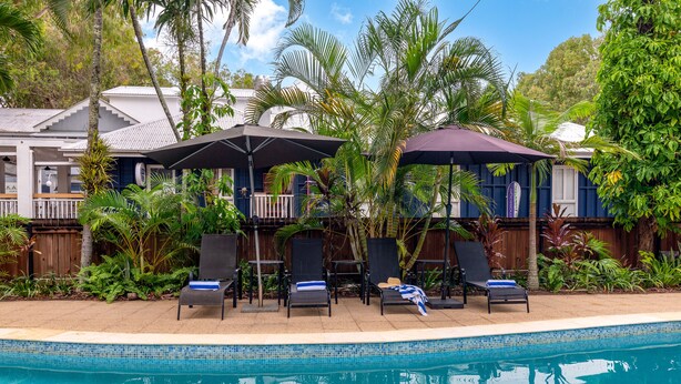 Un espace aménagé au bord de la piscine, avec des chaises longues, des parasols et une piscine à l’eau d’un bleu limpide.