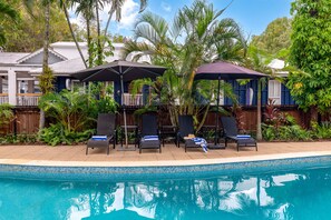Un espace aménagé au bord de la piscine, avec des chaises longues, des parasols et une piscine à l’eau d’un bleu limpide.