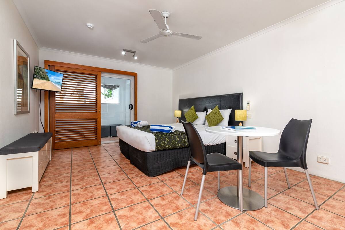 Ein Hotelzimmer mit einem Bett, einem Schreibtisch mit Stuhl, einem Fernseher und einem Deckenventilator.