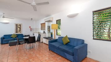 Una sala de estar moderna con un sofá azul, una mesa de comedor, sillas, ventiladores de techo y una ventana con persianas.