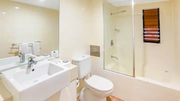 A modern bathroom with a white sink, mirror, toilet, and glass shower enclosure.