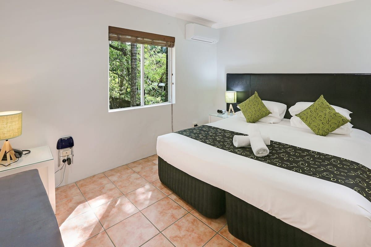 Une chambre d’hôtel équipée d’un lit, d’un bureau, d’une lampe, d’une fenêtre avec stores et d’un appareil de climatisation.