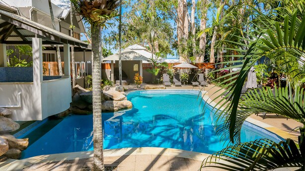 A swimming pool surrounded by palm trees and lounge chairs, with a building in the background. - Paradise on the Beach Resort - Palm Cove (Palm Cove)