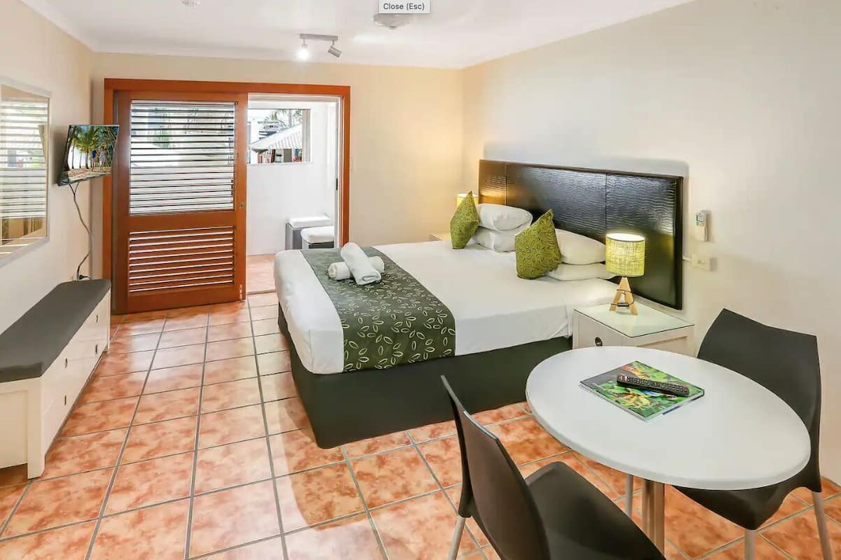 Ein Hotelzimmer mit Bett, Nachttisch, Lampe, Fernseher und einem kleinen Tisch mit Stühlen.