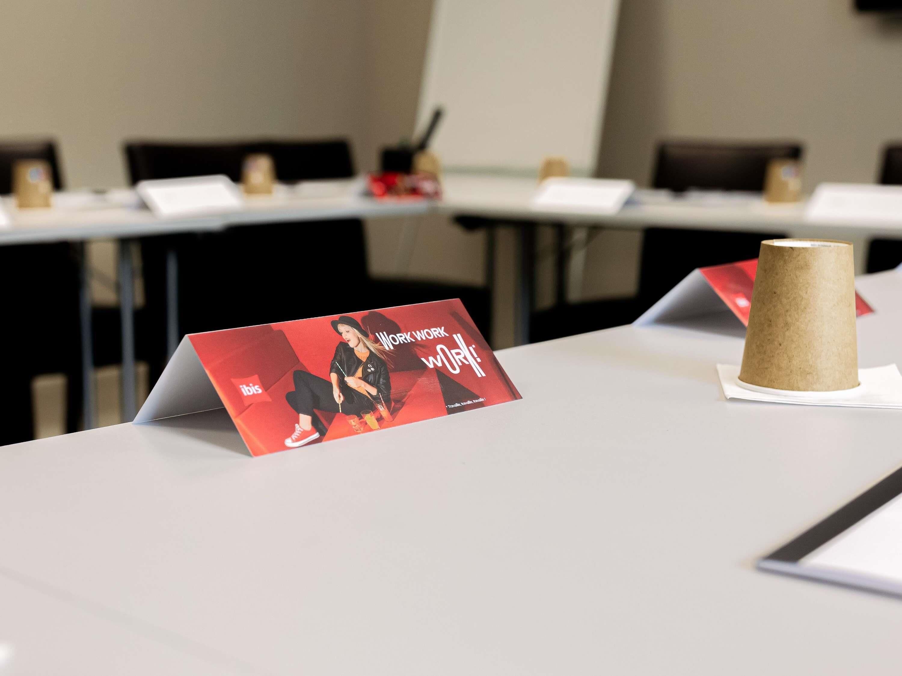 Un salón de conferencias con una mesa que muestra un cartel promocional, un vaso de papel y placas de identificación.