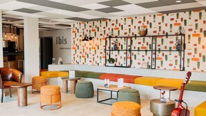Un hall d’entrée moderne avec un plafond à carreaux, des sièges aux couleurs vives et une guitare.