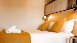 Un lit bien fait, avec des draps blancs, un plaid marron et deux oreillers.