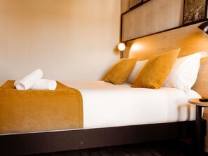 A neatly made bed with white linens, a brown throw blanket, and two pillows.