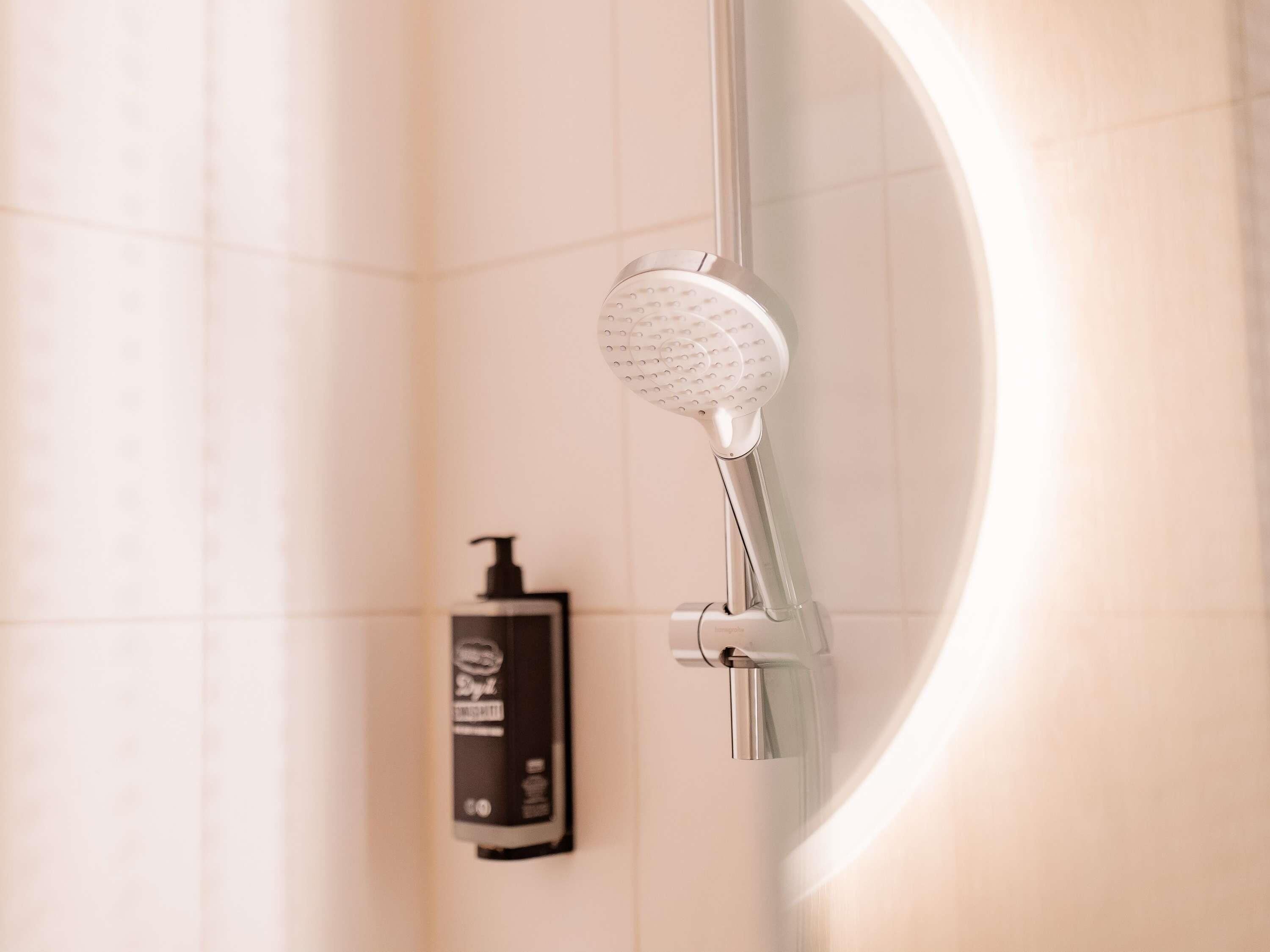 Une douche équipée d’un pommeau de douche à main, d’un distributeur de savon et d’un panneau de commande fixé au mur.