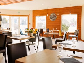 A restaurant with wooden walls, a clock, and multiple tables with chairs. - Ibis Clermont Ferrand A71 A75 La Meridienne (Clermont-Ferrand)