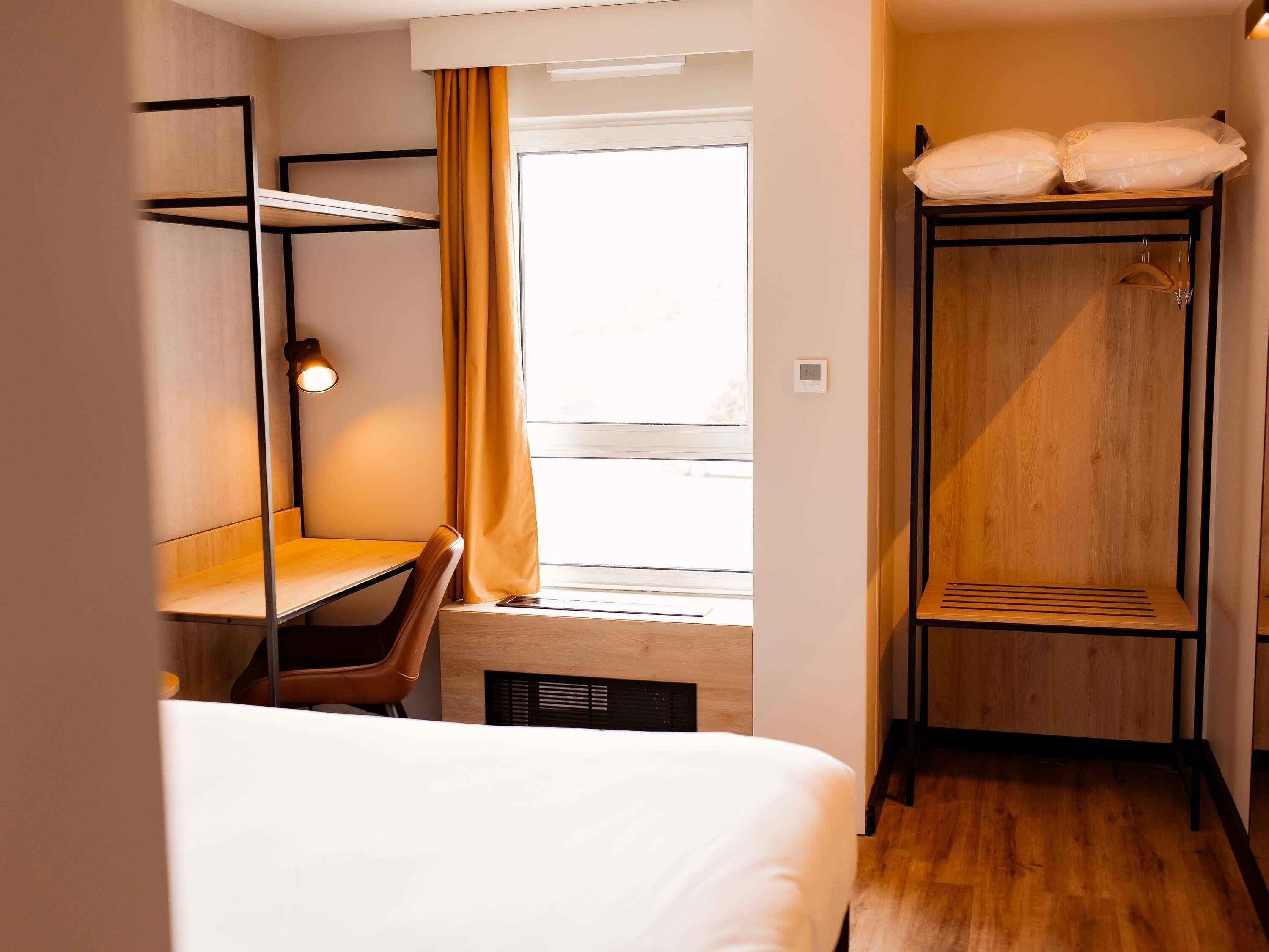 A hotel room with a bed, a desk, a chair, a wardrobe, and a window.