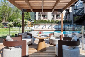 Um deck de madeira com área de estar externa, piscina e vista para as montanhas.